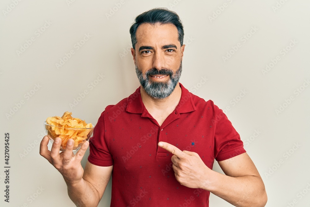 Middle age man with beard and grey hair holding potato chip smiling happy  pointing with hand and finger Stock Photo | Adobe Stock
