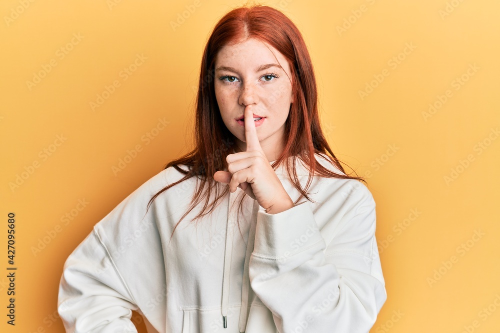 Young red head girl wearing casual sweatshirt asking to be quiet with finger on lips. silence and secret concept. Young red head girl wearing casual sweatshirt asking to be quiet with finger on lips. silence and secret concept.