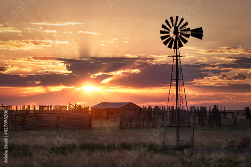 An old fashion windmill on a farm in a rural countryside landscape during sunset.
