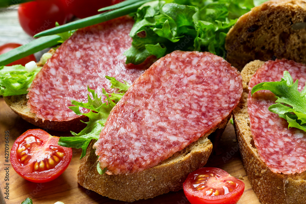 Sandwiches with dried sausage, tomatoes, onions on a cutting board. Sandwiches with dried sausage, tomatoes, onions on a cutting board.