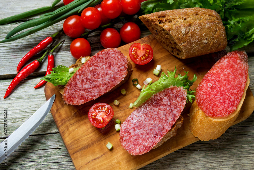 Sandwiches with dried sausage, tomatoes, onions on a cutting board. Sandwiches with dried sausage, tomatoes, onions on a cutting board.