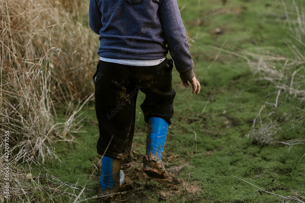 Cute little caucasian boy walking in nature wearing muddy blue gumboots Cute little caucasian boy walking in nature wearing muddy blue gumboots