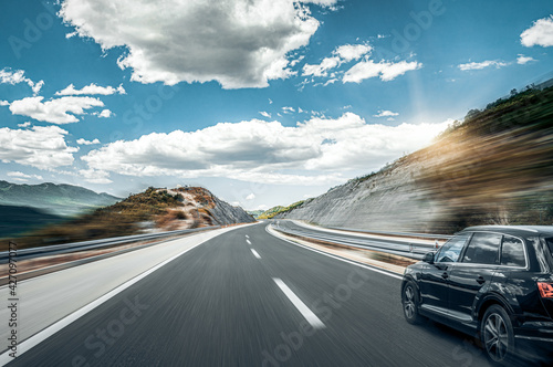Black car rushes along the road against the backdrop of a beautiful countryside landscape.