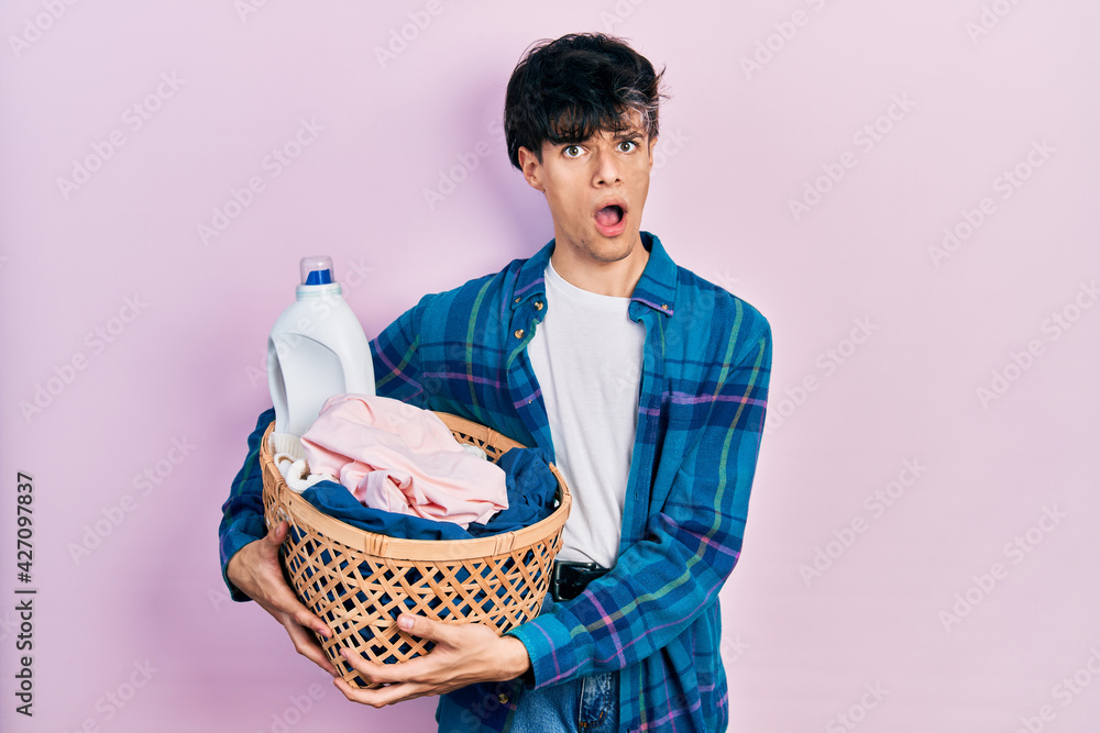 Handsome hipster young man holding laundry basket and detergent bottle in  shock face, looking skeptical and sarcastic, surprised with open mouth  Stock Photo | Adobe Stock