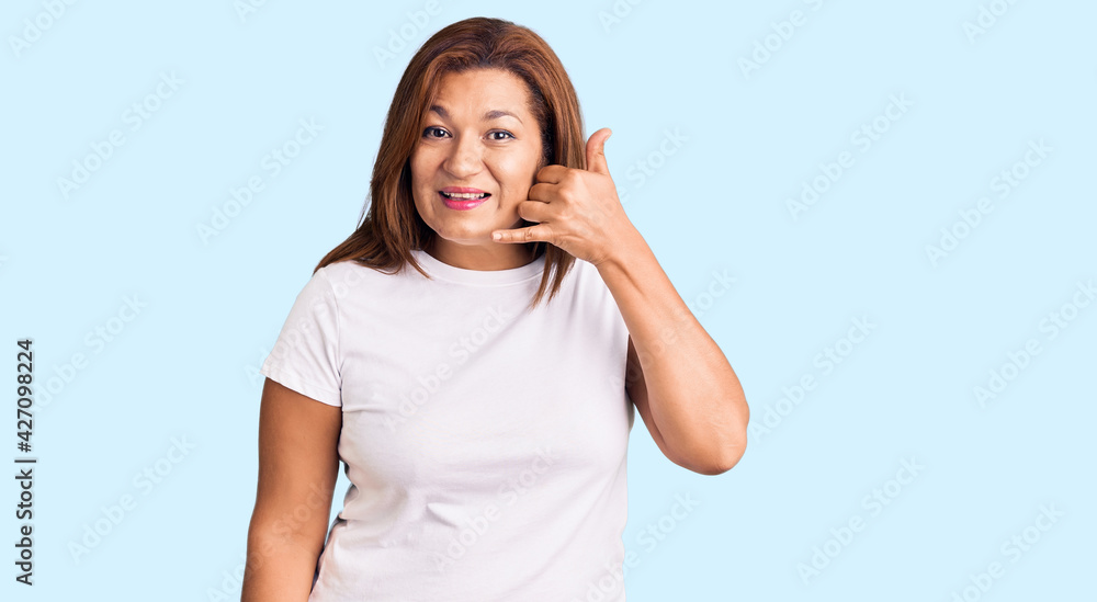 Middle age latin woman wearing casual white tshirt smiling doing phone gesture with hand and fingers like talking on the telephone. communicating concepts.