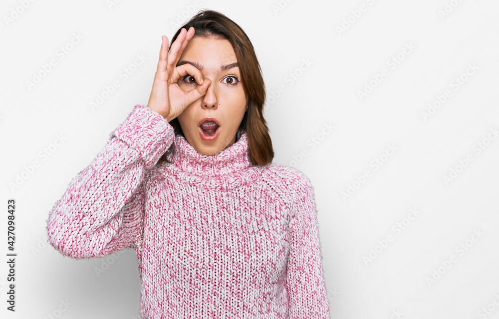 Young caucasian girl wearing wool winter sweater doing ok gesture shocked with surprised face, eye looking through fingers. unbelieving expression. Young caucasian girl wearing wool winter sweater doing ok gesture shocked with surprised face, eye looking through fingers. unbelieving expression.