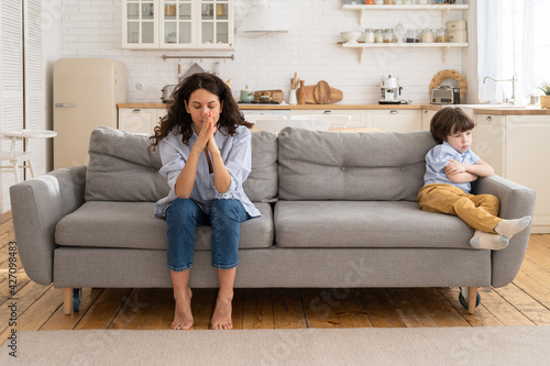 Valokuva Offended mom and son sit on couch in living room avoid talking and looking at each other after quarrel