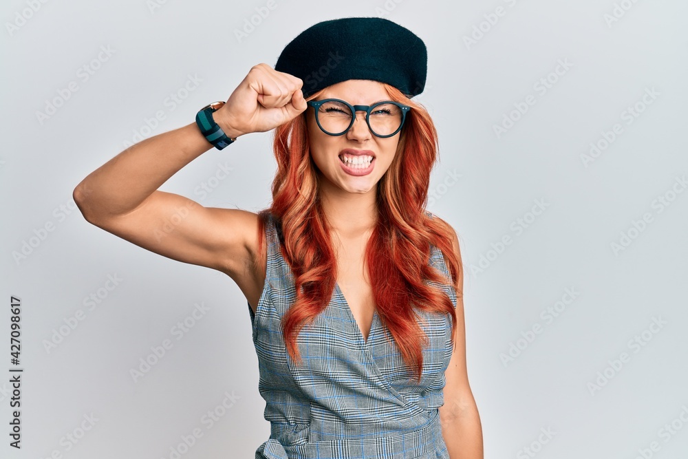 Naklejka premium Young redhead woman wearing fashion french look with beret angry and mad raising fist frustrated and furious while shouting with anger. rage and aggressive concept.