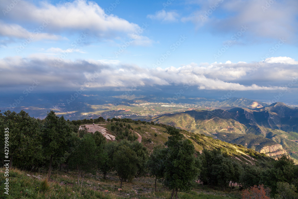 Aerial view of the Montserrat mountains on a beautiful spring day, Catalonia, Spain. Dramatic sky over the mountains. Sunlight falls through the clouds on the ground and mountains.