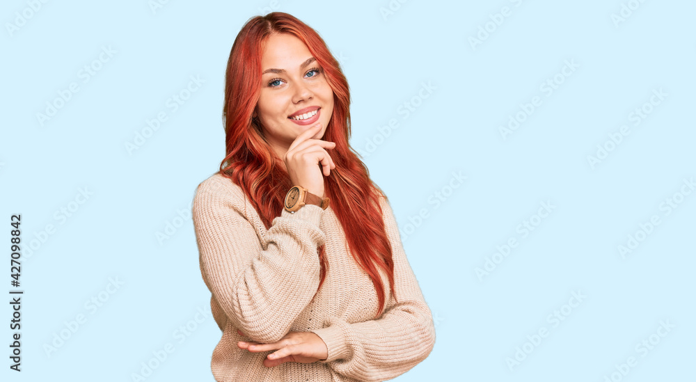 Young redhead woman wearing casual winter sweater looking confident at the camera smiling with crossed arms and hand raised on chin. thinking positive. Young redhead woman wearing casual winter sweater looking confident at the camera smiling with crossed arms and hand raised on chin. thinking positive.