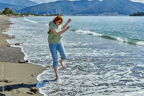 Barefoot young woman tries to walk on cool water in surf zone in early spring in Fethiye, Turkey.