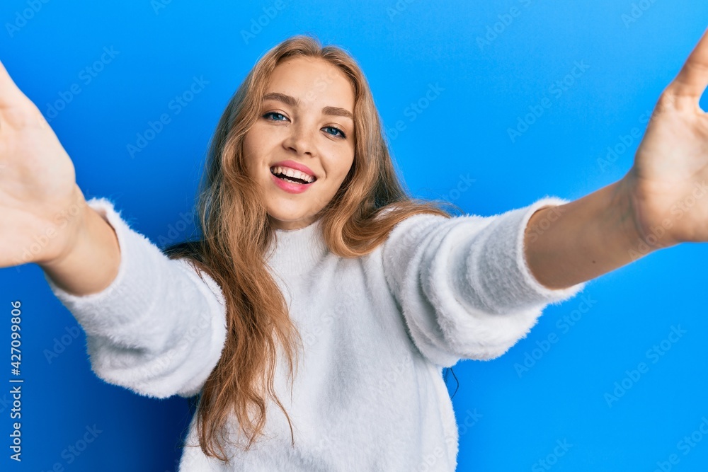 Fototapeta premium Beautiful blonde caucasian woman wearing casual winter sweater looking at the camera smiling with open arms for hug. cheerful expression embracing happiness.