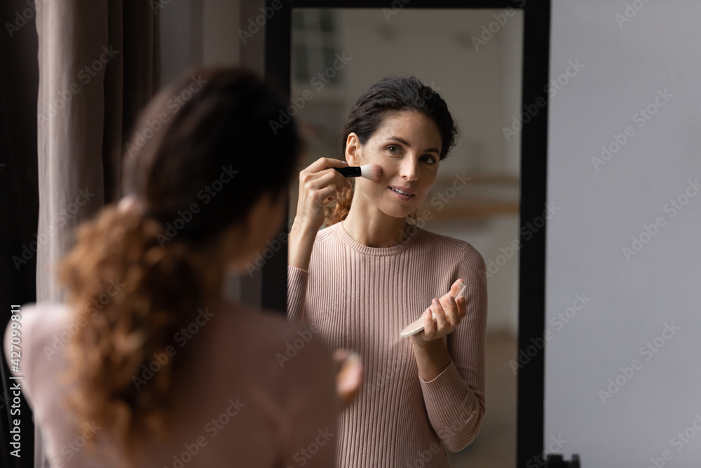 Morning make up. Charming latin female look at mirror hold powder compact container put flour on face with big brush. Happy young woman enjoy visage use professional color cosmetic pressed dry blusher - obrazy, fototapety, plakaty 