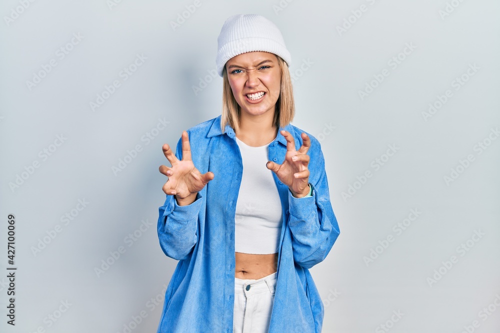 Beautiful blonde woman wearing wool hat smiling funny doing claw gesture as cat, aggressive and sexy expression Beautiful blonde woman wearing wool hat smiling funny doing claw gesture as cat, aggressive and sexy expression