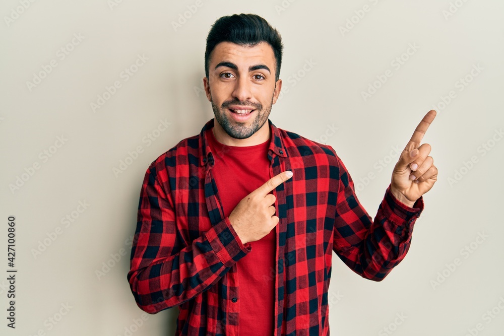 Young hispanic man wearing casual clothes smiling and looking at the camera pointing with two hands and fingers to the side. Young hispanic man wearing casual clothes smiling and looking at the camera pointing with two hands and fingers to the side.