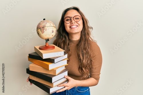 Photo Young hispanic girl studying geography smiling with a happy and cool smile on face