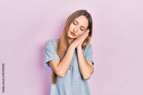 Young blonde girl wearing casual t shirt sleeping tired dreaming and posing with hands together while smiling with closed eyes. © Krakenimages.com