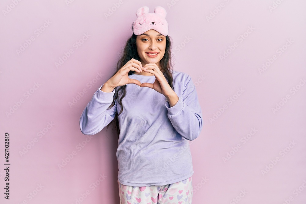 Beautiful middle eastern woman wearing sleep mask and pajama smiling in love showing heart symbol and shape with hands. romantic concept. Beautiful middle eastern woman wearing sleep mask and pajama smiling in love showing heart symbol and shape with hands. romantic concept.