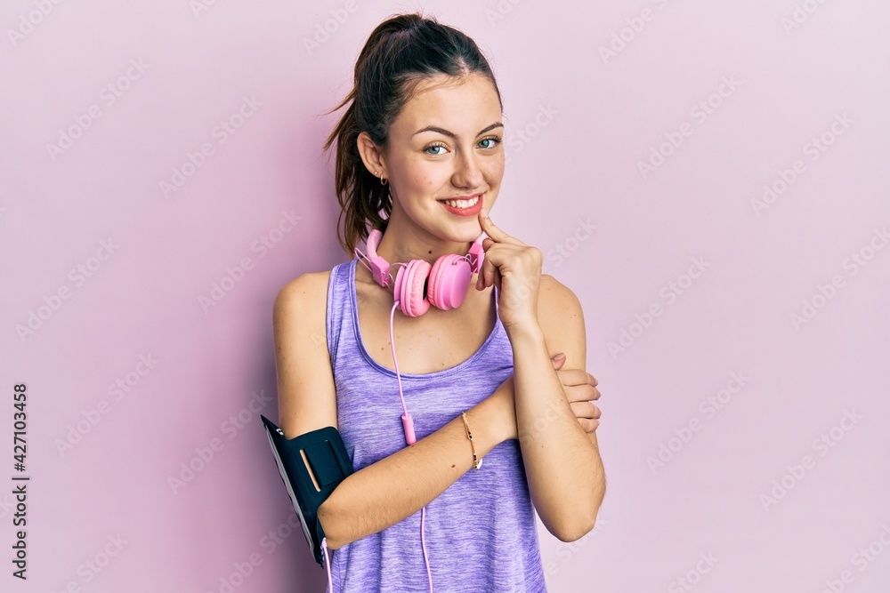Young brunette woman wearing sportswear and headphones smiling looking confident at the camera with crossed arms and hand on chin. thinking positive. Young brunette woman wearing sportswear and headphones smiling looking confident at the camera with crossed arms and hand on chin. thinking positive.