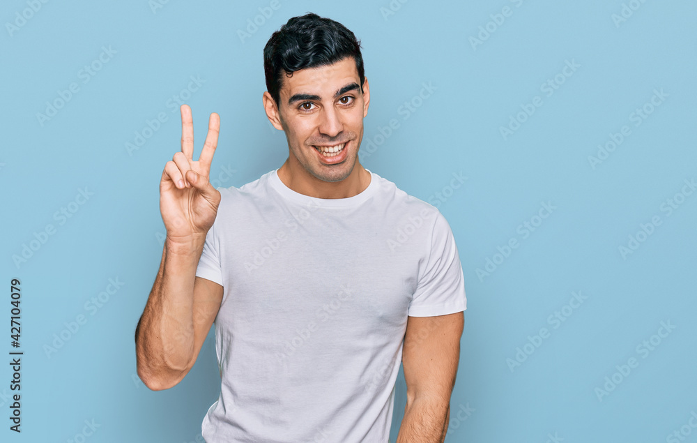 Handsome hispanic man wearing casual white t shirt showing and pointing up with fingers number two while smiling confident and happy. Handsome hispanic man wearing casual white t shirt showing and pointing up with fingers number two while smiling confident and happy.