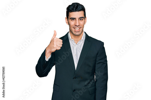 Handsome hispanic man wearing business clothes doing happy thumbs up gesture with hand. approving expression looking at the camera showing success.