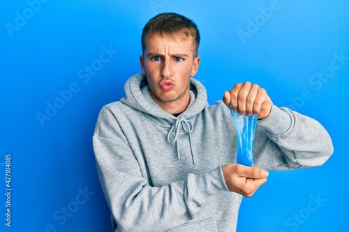 Young caucasian man holding slime making fish face with mouth and squinting eyes, crazy and comical.