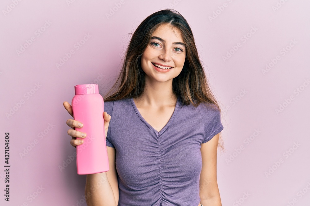 Young caucasian woman holding shampoo bottle looking positive and happy standing and smiling with a confident smile showing teeth Young caucasian woman holding shampoo bottle looking positive and happy standing and smiling with a confident smile showing teeth