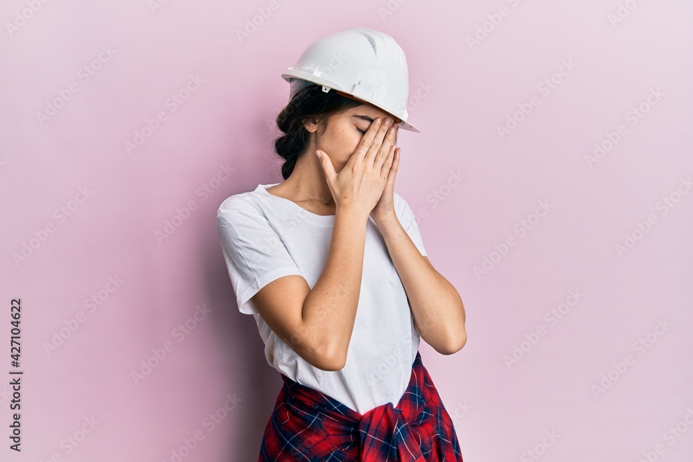 Young caucasian woman wearing hardhat with sad expression covering face with hands while crying. depression concept. Young caucasian woman wearing hardhat with sad expression covering face with hands while crying. depression concept.