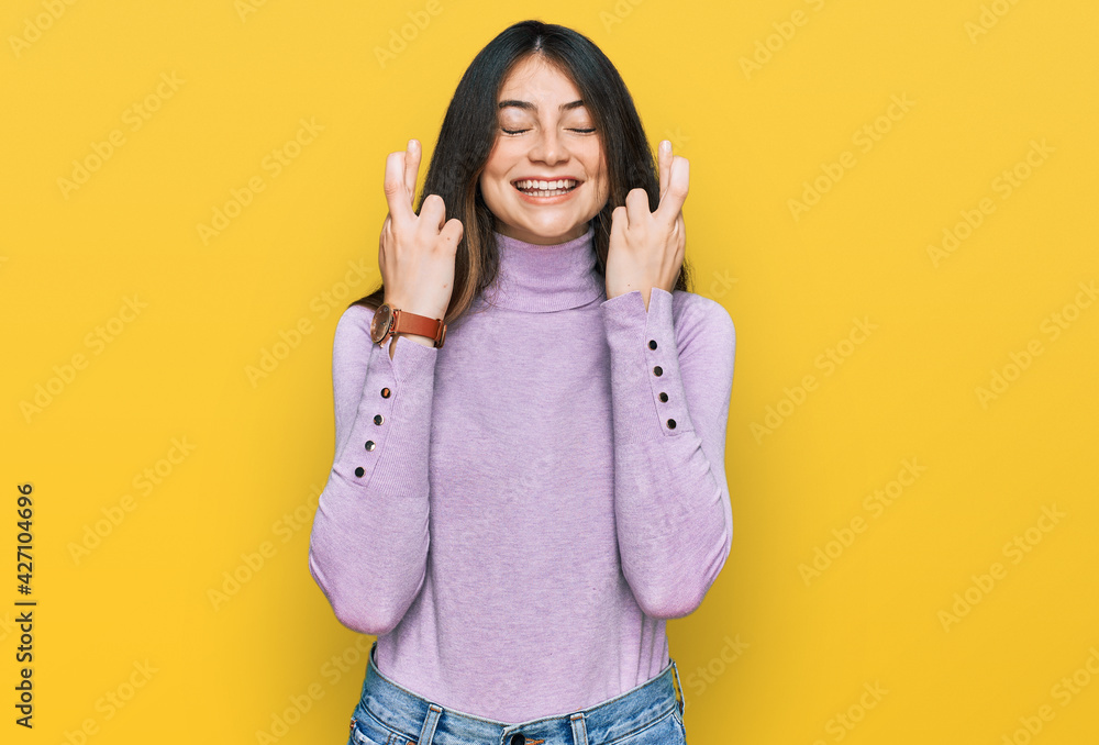 Young beautiful teen girl wearing turtleneck sweater gesturing finger crossed smiling with hope and eyes closed. luck and superstitious concept. Young beautiful teen girl wearing turtleneck sweater gesturing finger crossed smiling with hope and eyes closed. luck and superstitious concept.