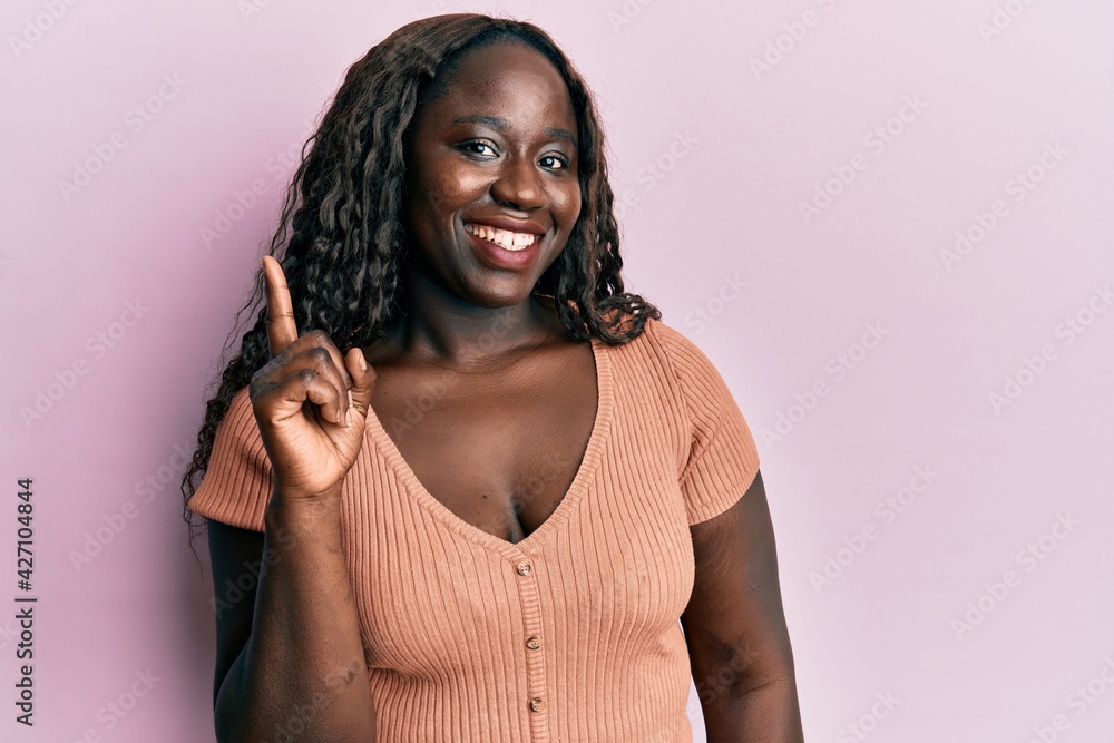 African young woman wearing casual clothes smiling with an idea or question pointing finger up with happy face, number one African young woman wearing casual clothes smiling with an idea or question pointing finger up with happy face, number one