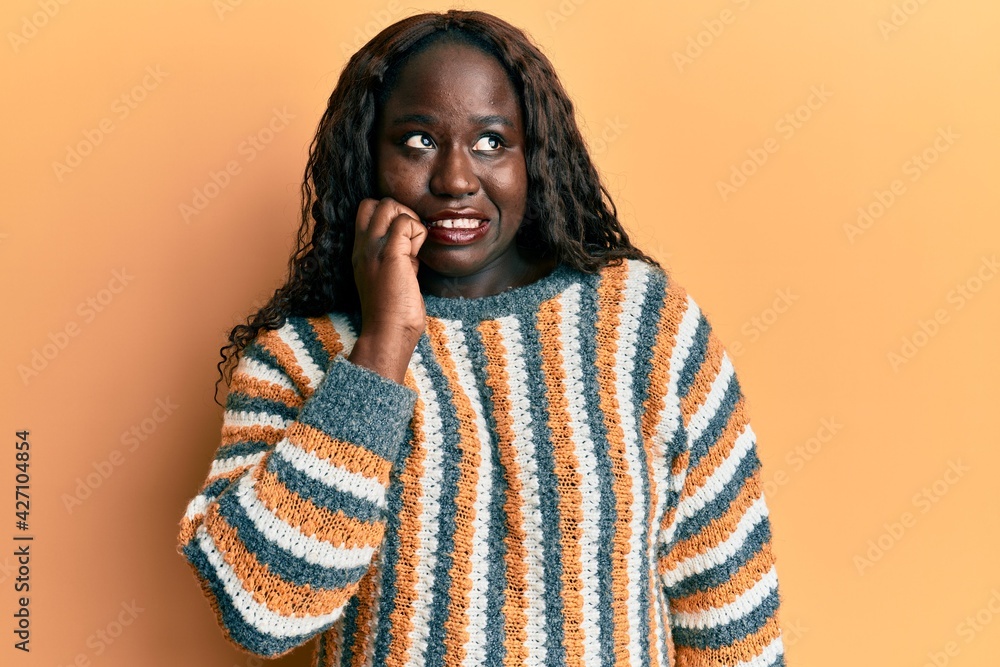 African young woman wearing wool winter sweater looking stressed and nervous with hands on mouth biting nails. anxiety problem. African young woman wearing wool winter sweater looking stressed and nervous with hands on mouth biting nails. anxiety problem.
