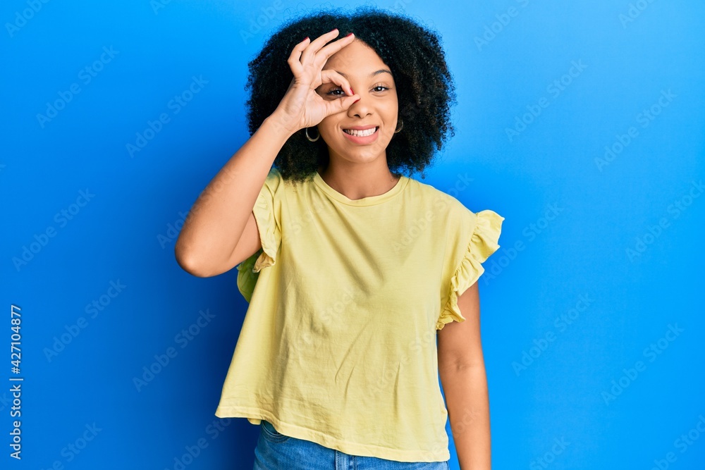 Young african american girl wearing casual clothes doing ok gesture with hand smiling, eye looking through fingers with happy face. Young african american girl wearing casual clothes doing ok gesture with hand smiling, eye looking through fingers with happy face.