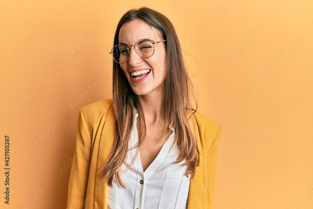 Young beautiful woman wearing business style and glasses winking looking at the camera with sexy expression, cheerful and happy face.