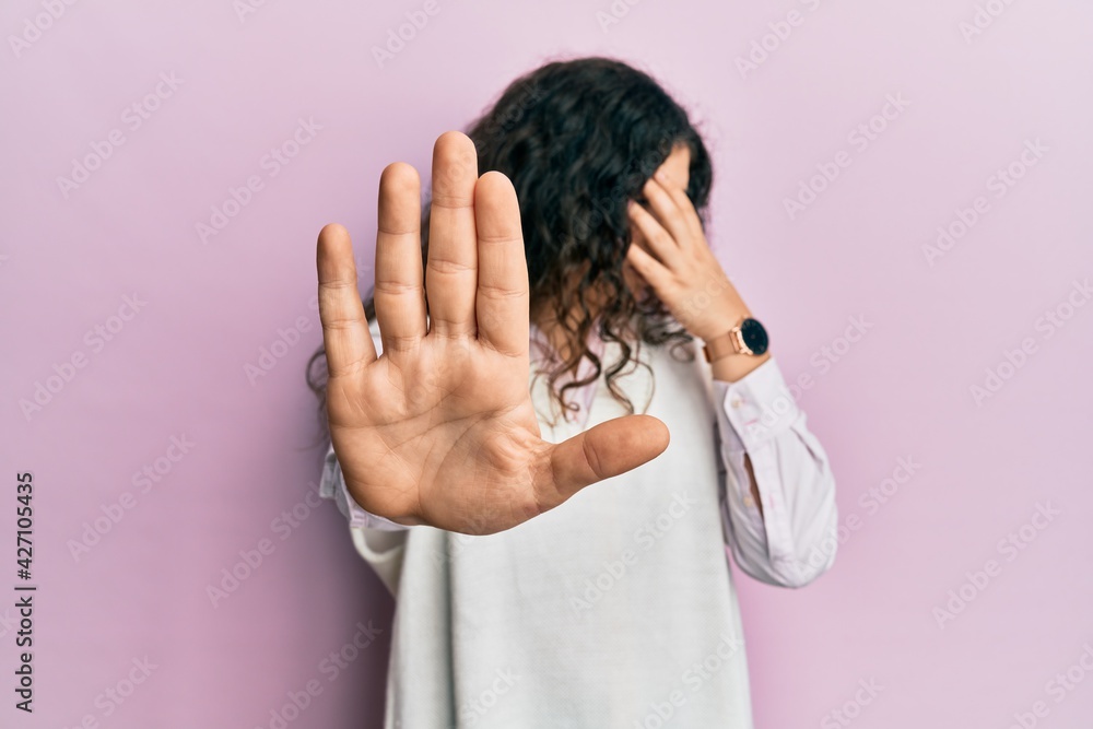 Young brunette woman with curly hair wearing casual clothes covering eyes with hands and doing stop gesture with sad and fear expression. embarrassed and negative concept. Young brunette woman with curly hair wearing casual clothes covering eyes with hands and doing stop gesture with sad and fear expression. embarrassed and negative concept.