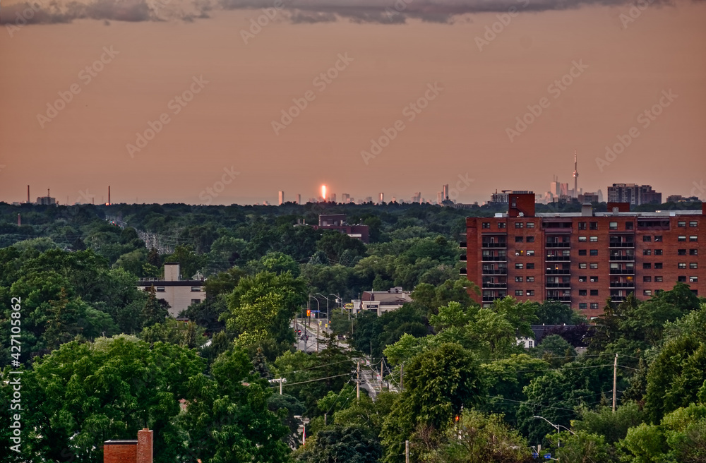 The Toronto skyline with the CN tower seen in the distance from the west as the sun sets on a sping day over a lush urban forest