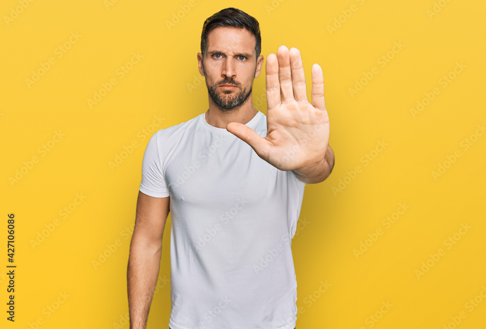 Handsome man with beard wearing casual white t shirt doing stop sing with palm of the hand. warning expression with negative and serious gesture on the face. Handsome man with beard wearing casual white t shirt doing stop sing with palm of the hand. warning expression with negative and serious gesture on the face.