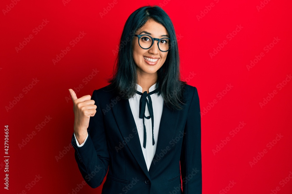Beautiful asian young woman wearing business suit smiling with happy face looking and pointing to the side with thumb up. Beautiful asian young woman wearing business suit smiling with happy face looking and pointing to the side with thumb up.