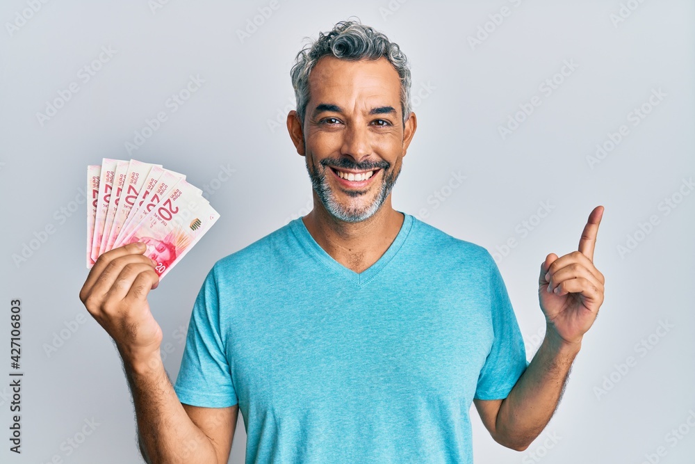 Middle age grey-haired man holding israel shekels smiling happy pointing with hand and finger to the side Middle age grey-haired man holding israel shekels smiling happy pointing with hand and finger to the side