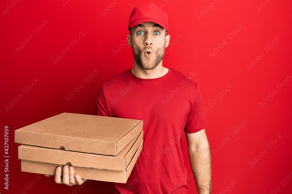 Young caucasian man holding delivery pizza box scared and amazed with open mouth for surprise, disbelief face Young caucasian man holding delivery pizza box scared and amazed with open mouth for surprise, disbelief face
