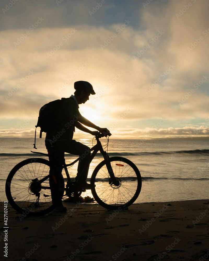 Obraz premium Silhouette image of a cyclist getting ready to ride on the beach at sunrise. Vertical format.