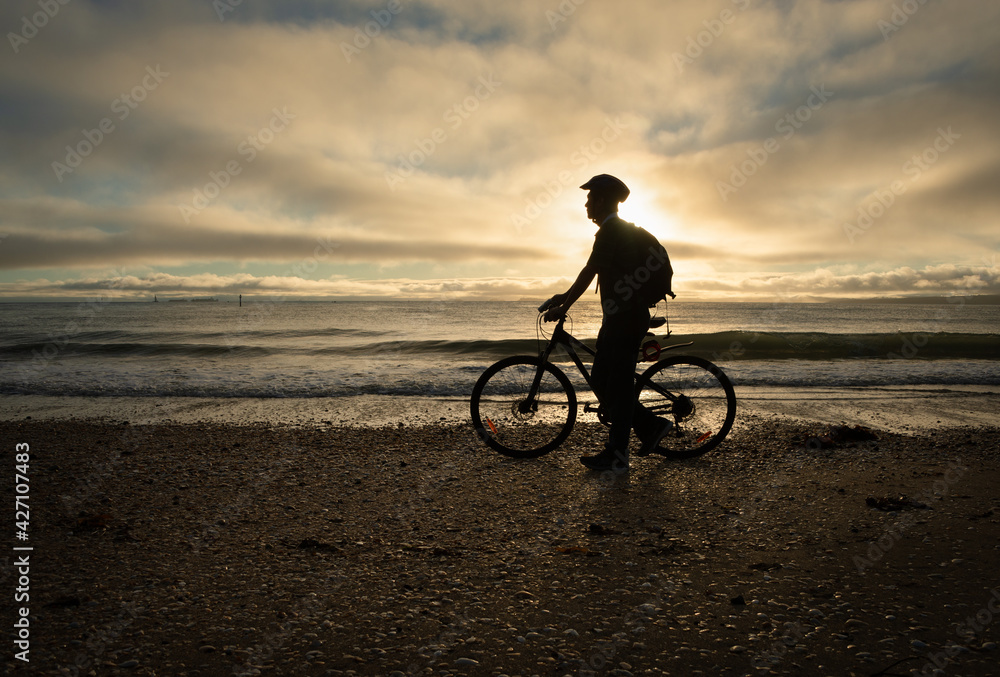 Obraz premium Silhouette image of a cyclist walking and pushing the bike on the beach at sunrise