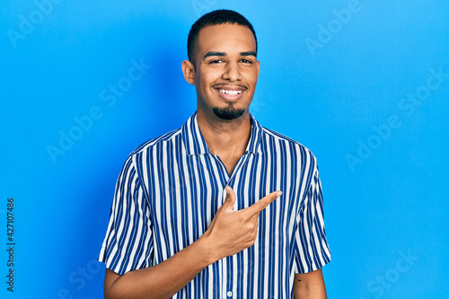 Young african american man wearing casual clothes cheerful with a smile of face pointing with hand and finger up to the side with happy and natural expression on face