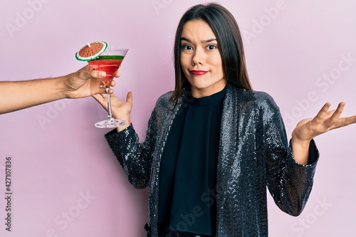 Canvas Print Young girl wearing sexy party jacket and hispanic arm offering cocktail clueless and confused with open arms, no idea and doubtful face
