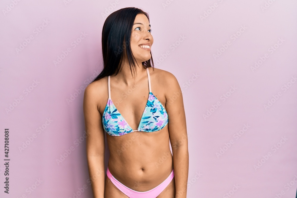 Fototapeta premium Young latin woman wearing bikini looking away to side with smile on face, natural expression. laughing confident.