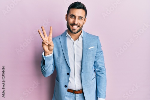 Young hispanic businessman wearing business jacket showing and pointing up with fingers number three while smiling confident and happy.