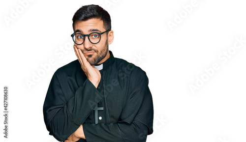 Young hispanic man wearing priest uniform thinking looking tired and bored with depression problems with crossed arms. © Krakenimages.com