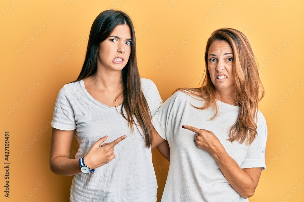 Hispanic family of mother and daughter wearing casual white tshirt pointing aside worried and nervous with forefinger, concerned and surprised expression Hispanic family of mother and daughter wearing casual white tshirt pointing aside worried and nervous with forefinger, concerned and surprised expression