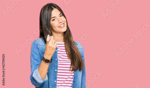 Young brunette woman wearing casual clothes beckoning come here gesture with hand inviting welcoming happy and smiling