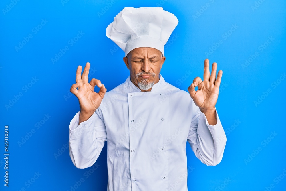 Middle age grey-haired man wearing professional cook uniform and hat relax and smiling with eyes closed doing meditation gesture with fingers. yoga concept. Middle age grey-haired man wearing professional cook uniform and hat relax and smiling with eyes closed doing meditation gesture with fingers. yoga concept.