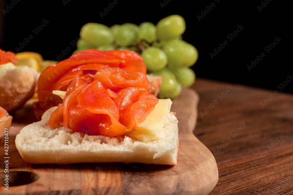 Smoked salmon sandwich with cheese and green grapes on a wooden board. Close up, Selective focus. Black background. Smoked salmon sandwich with cheese and green grapes on a wooden board. Close up, Selective focus. Black background.